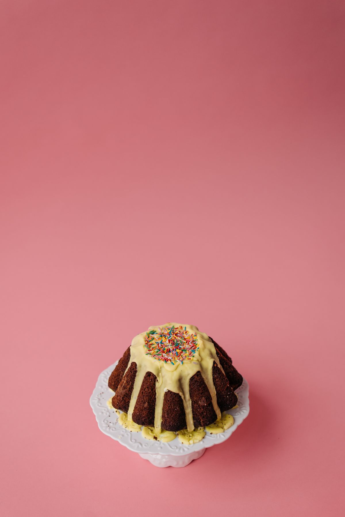 Foto ilustrativa de bolo de chocolate com cobertura clara em fundo rosa